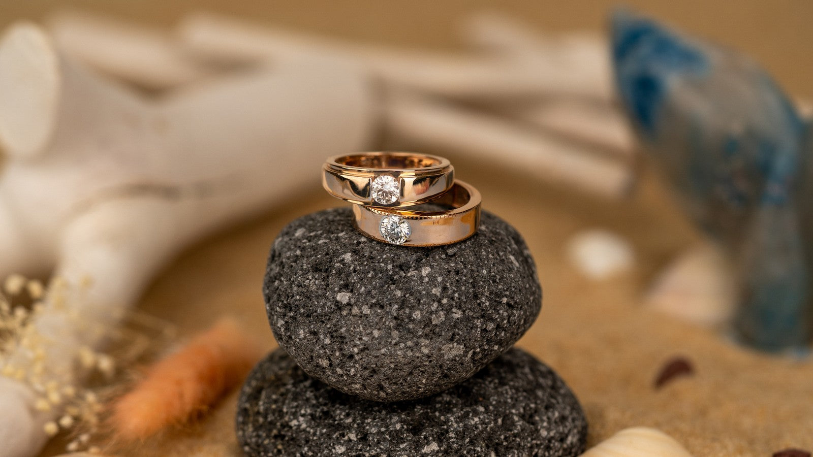 Pair of rose gold couple rings, each set with a diamond, stacked on a stone