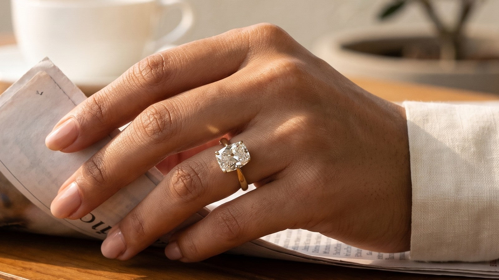 Cushion cut lab grown diamond solitaire in yellow gold, worn while turning the morning newspaper