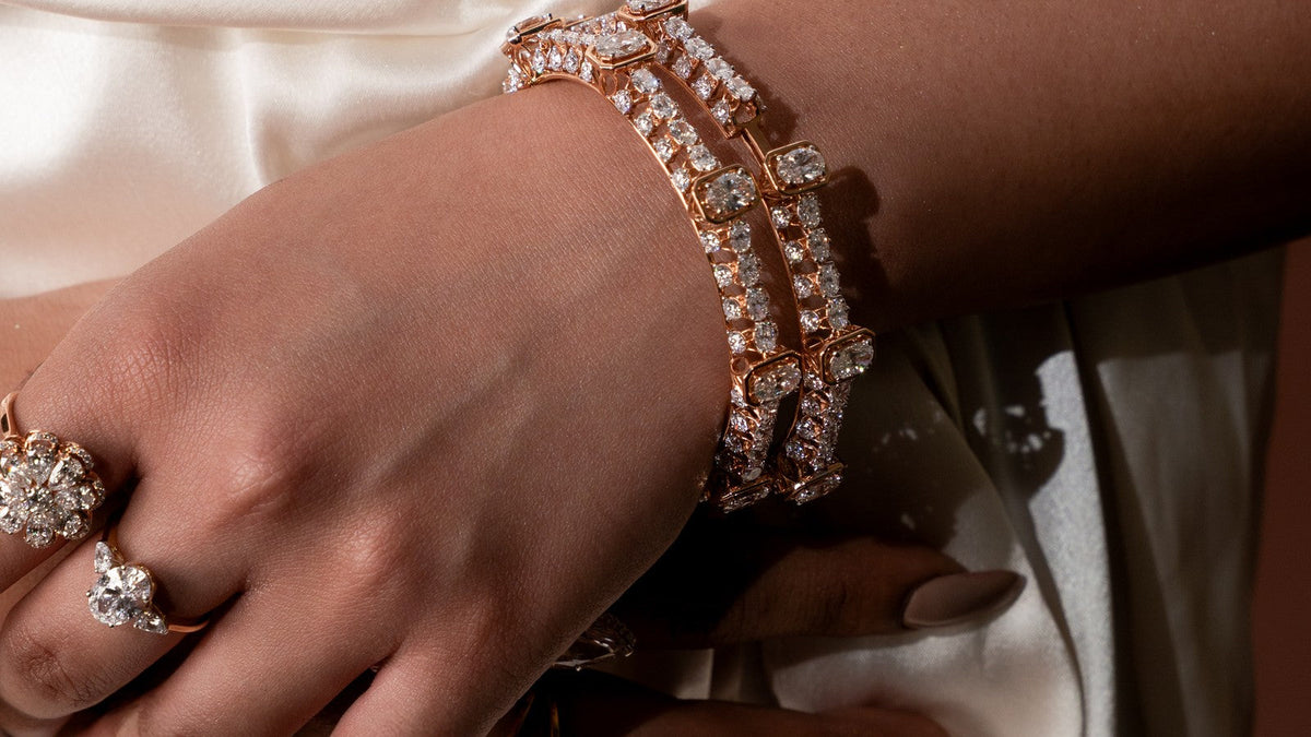 Stack of rose gold diamond bangles worn on the wrist over an ivory satin dress