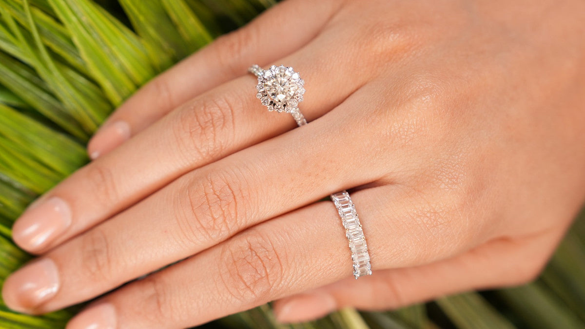 Baguette eternity band worn beside a halo diamond ring, hand resting on palm leaves
