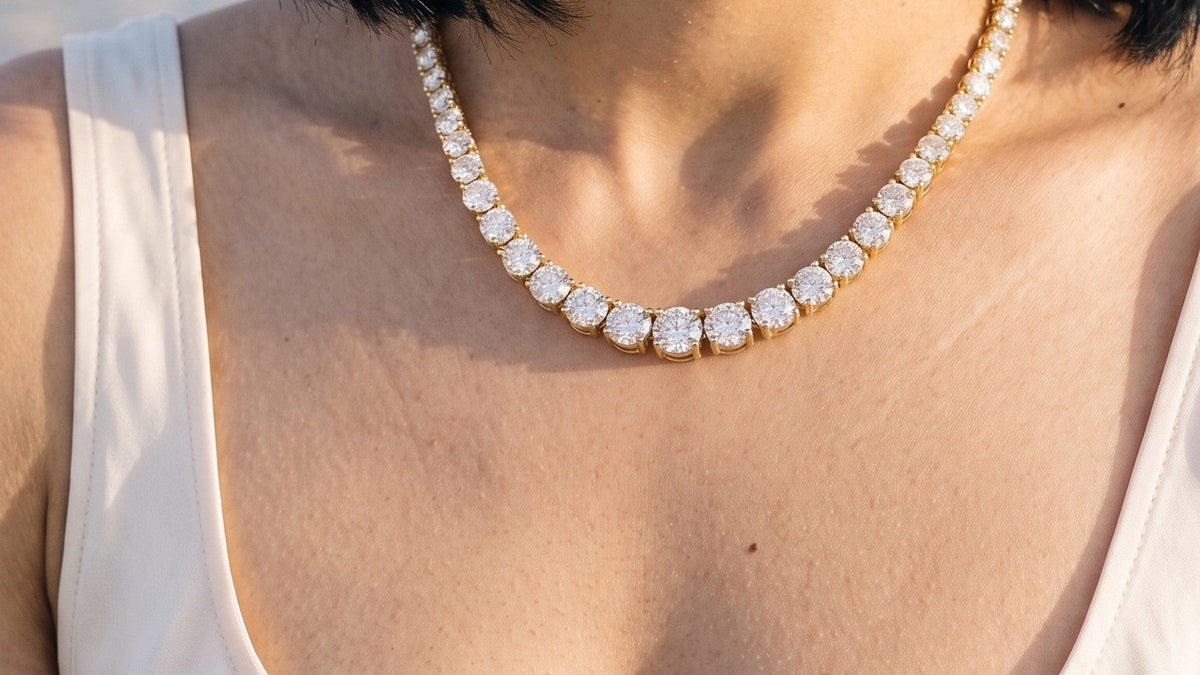 A woman wearing a diamond tennis necklace, close at the collarbone, in warm evening light