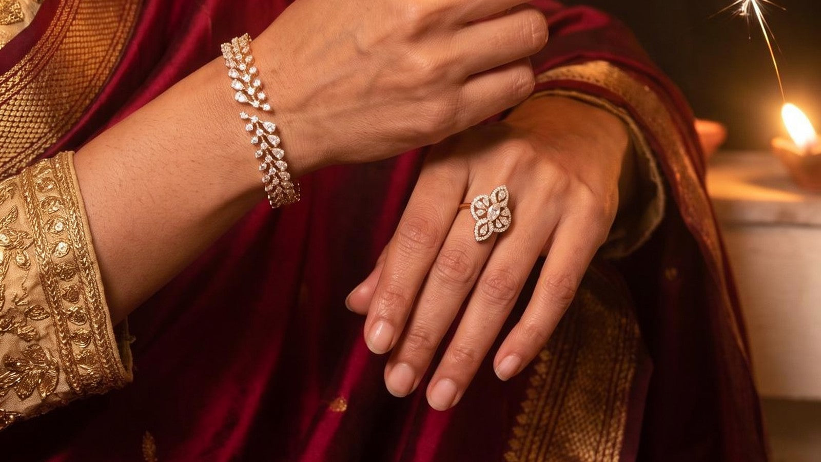 A diamond bracelet and ring on a woman's hands, a diya and a sparkler glowing behind