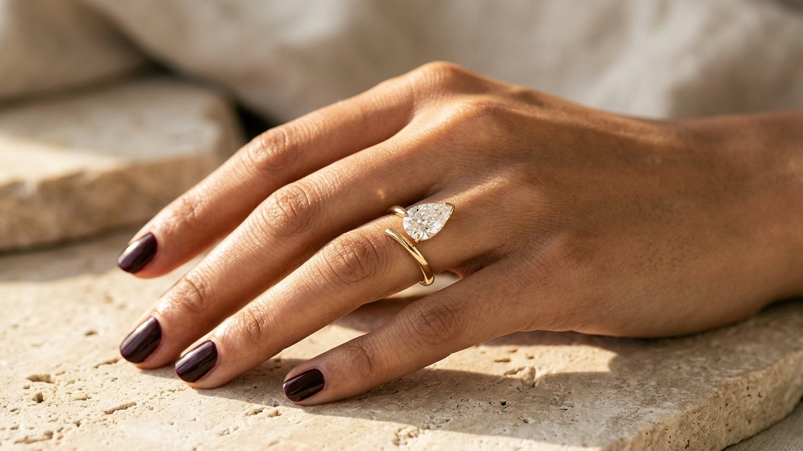 Pear lab grown diamond ring stacked with a plain gold band on a sunlit hand