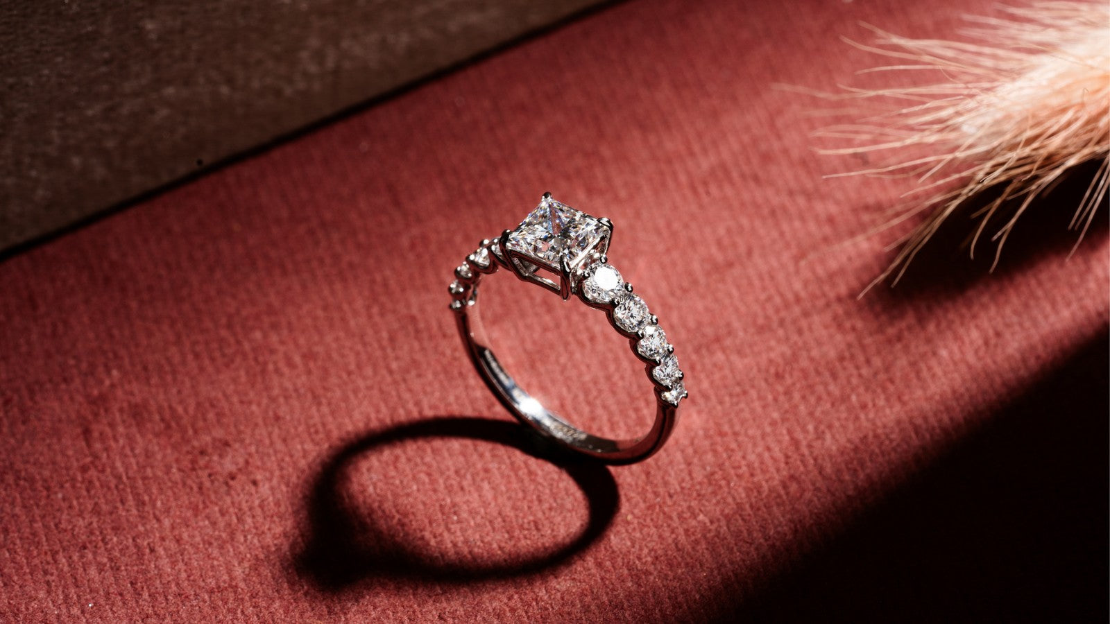 Princess cut lab grown diamond ring with a row of round side stones on warm red velvet