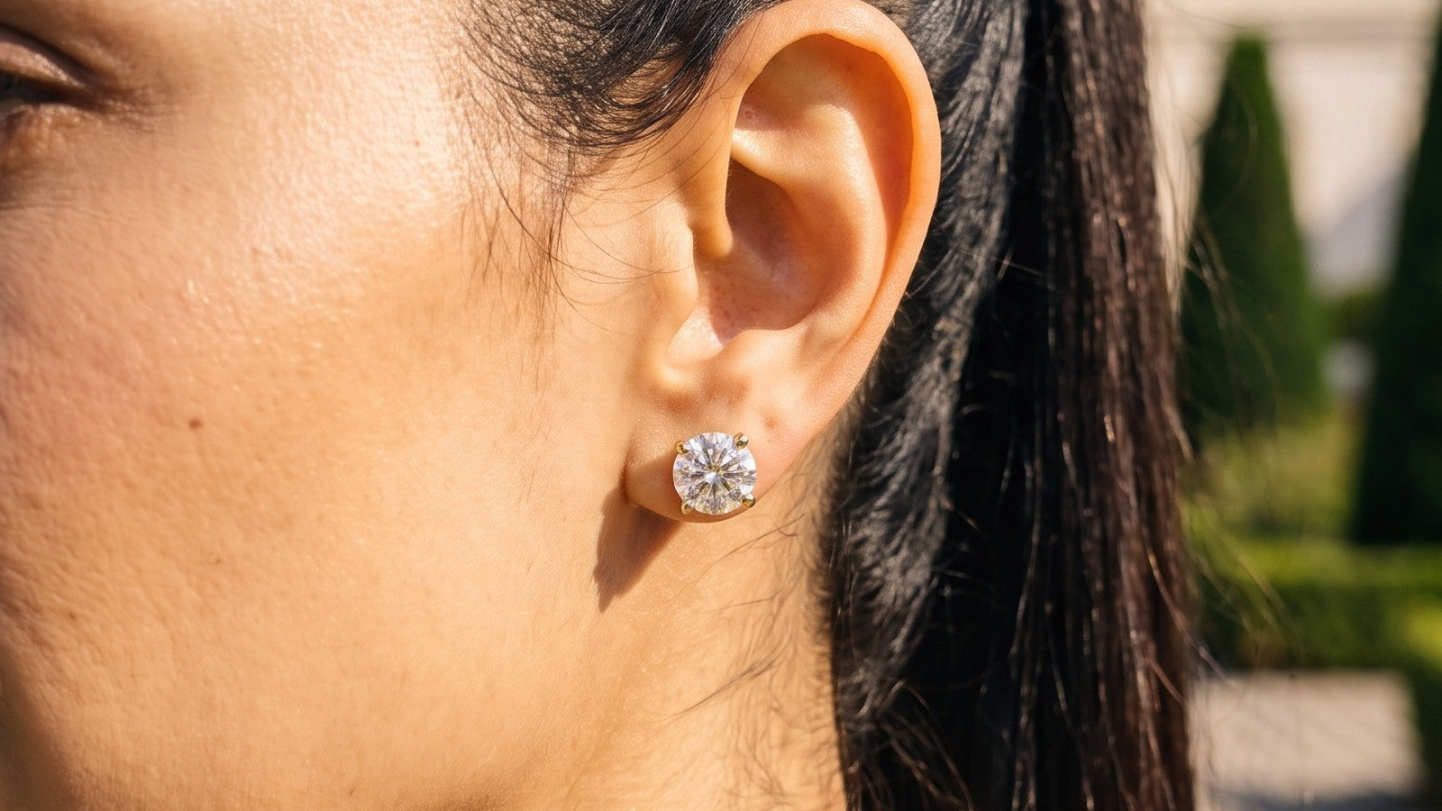 A round diamond solitaire stud earring, seen in profile in soft garden light